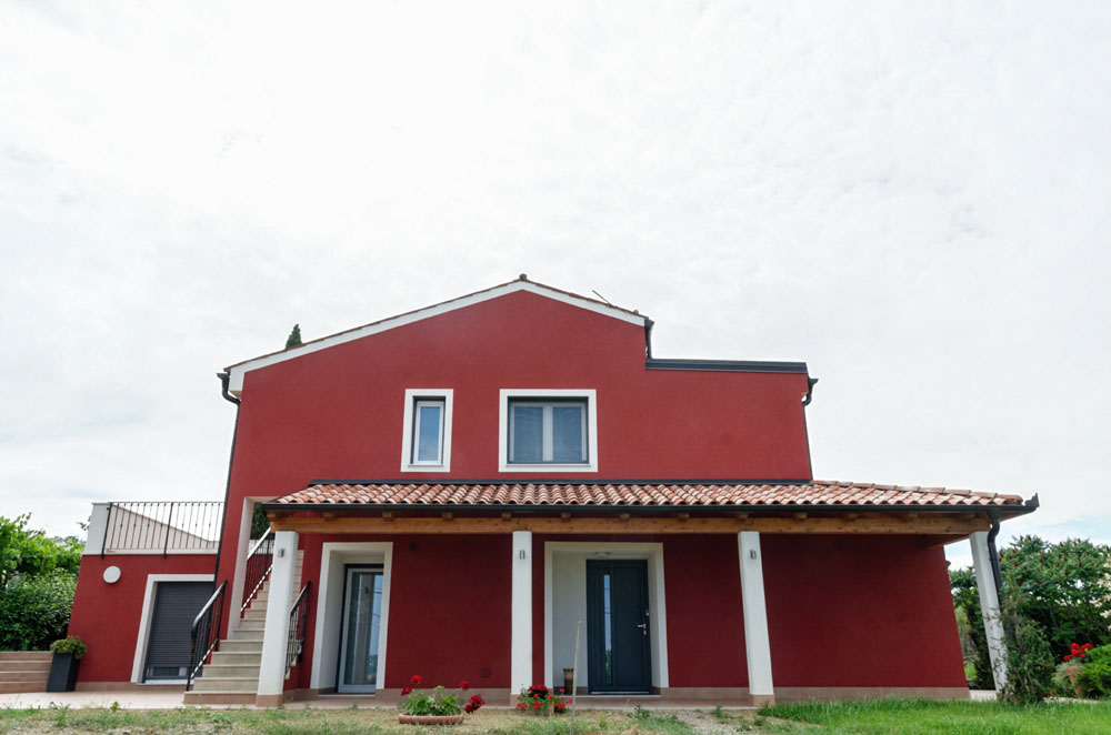 Rdeča hiša z okni in vrati v antracit barvi.